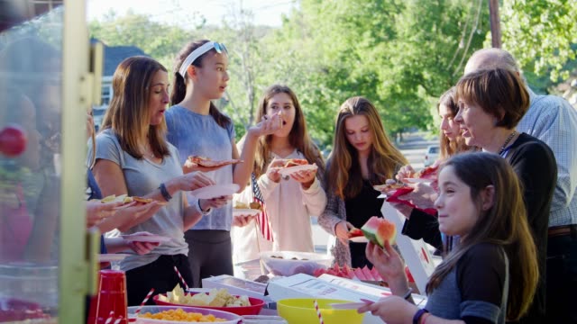 Neighbours stand eating around a table at a block party